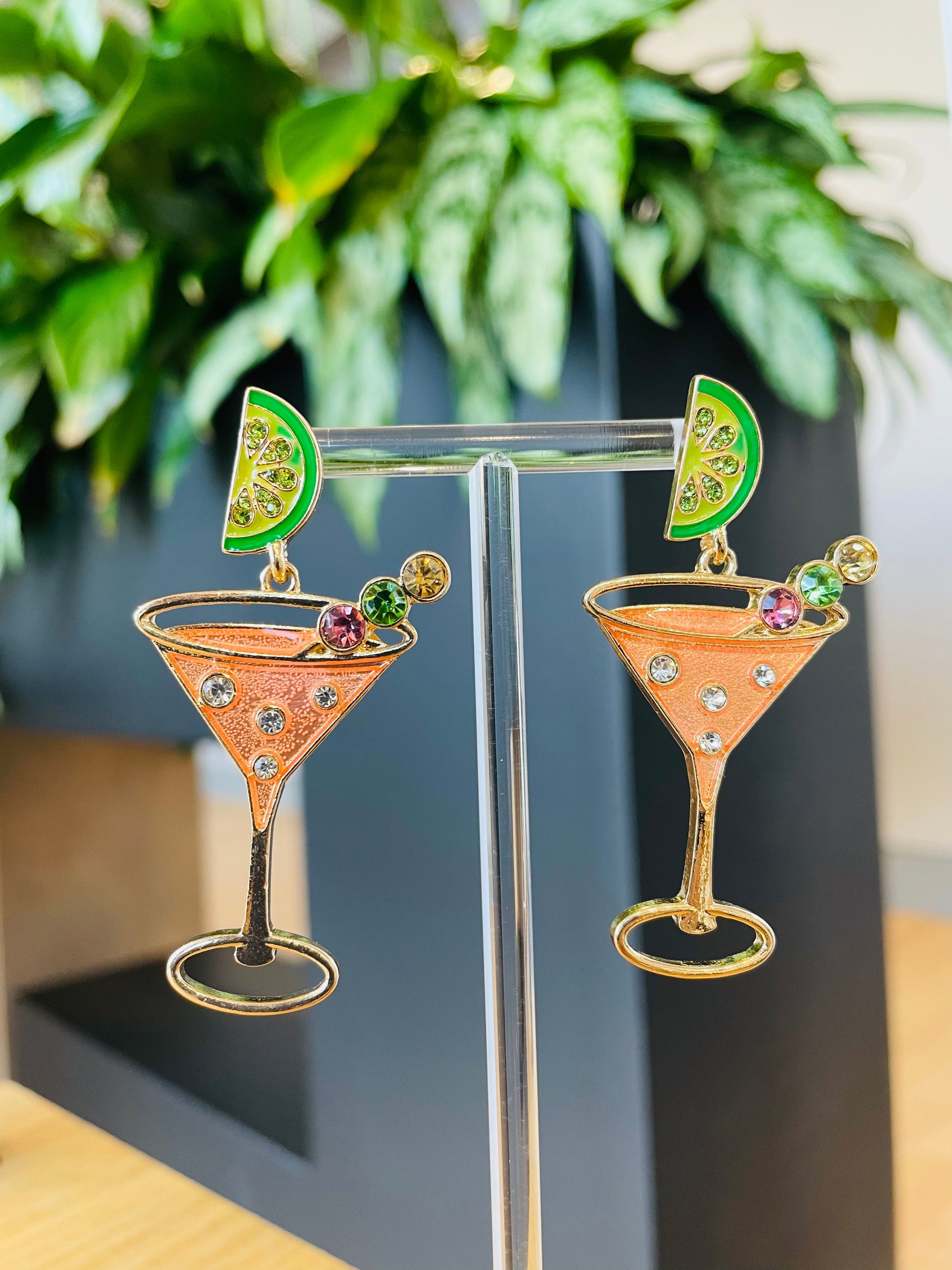 A pair of Aperol Spritz themed earrings displayed on a stand, featuring a martini glass shape with orange and green accents.