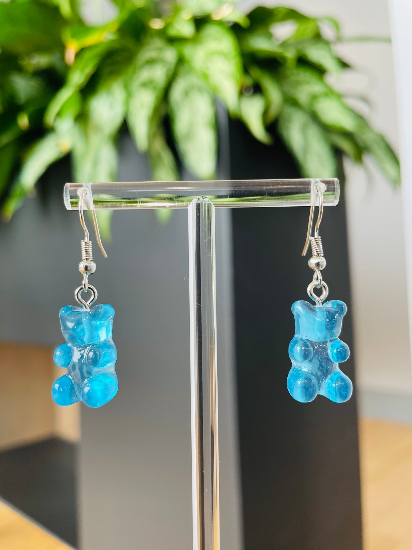 A pair of blue candy-shaped earrings displayed on an ear stand, with a blurred background featuring green foliage.