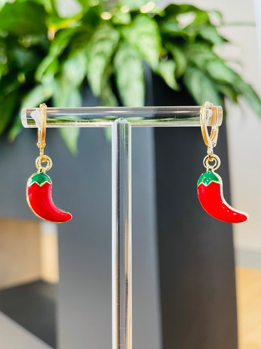 A pair of red chili pepper earrings on a display stand against a blurred background with a green plant.