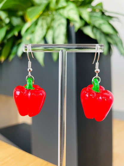 A pair of vibrant red bell pepper earrings displayed on an earring stand, with green accents representing the stem.
