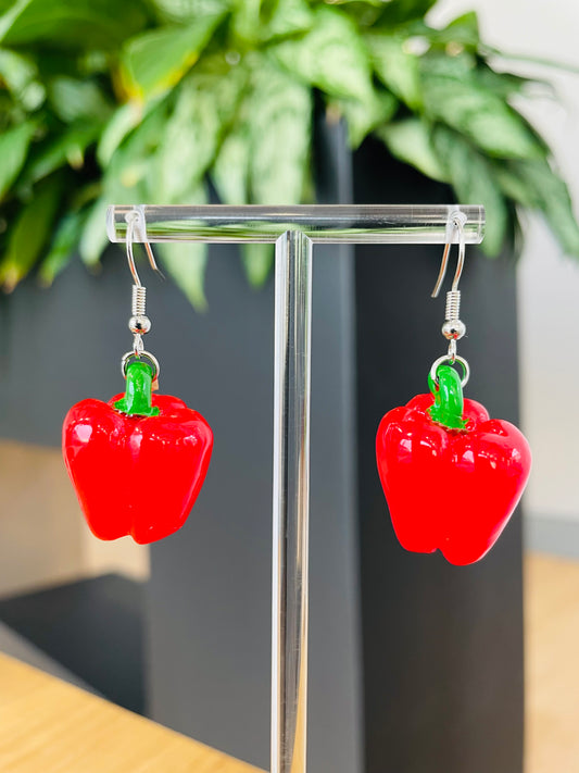 A pair of vibrant red bell pepper earrings displayed on an earring stand, with green accents representing the stem.