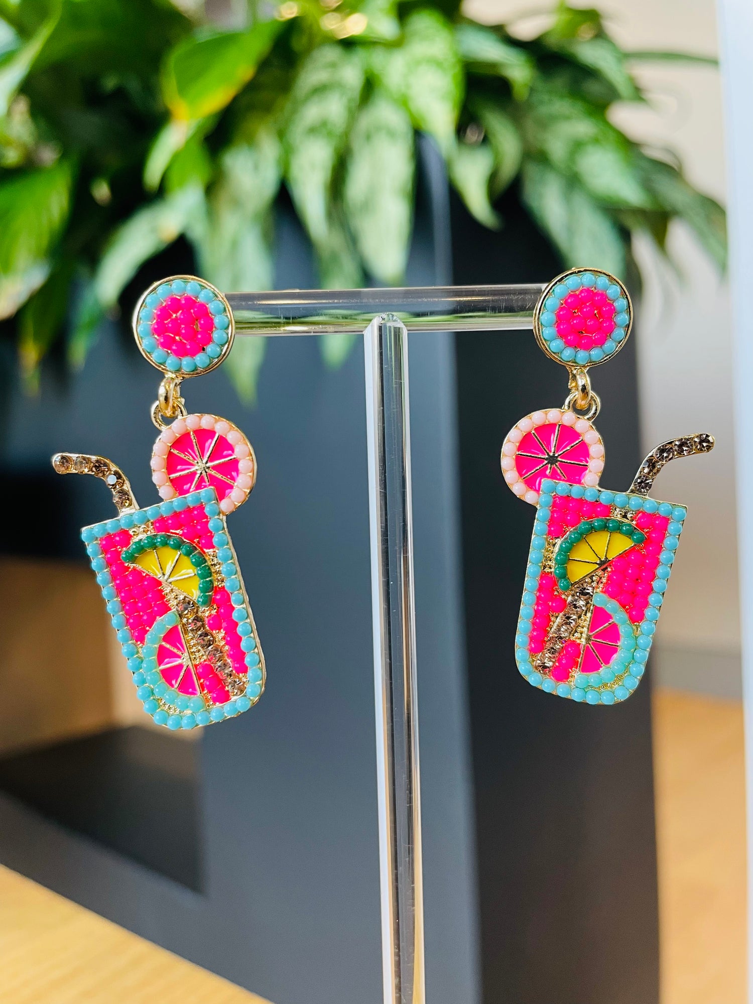 A pair of pink and green cocktail earrings with a tropical design, displayed on a stand. Playful Pantry 