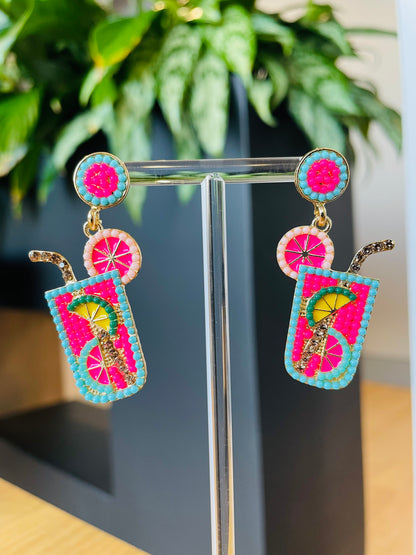 A pair of pink and green cocktail earrings with a tropical design, displayed on a stand. Playful Pantry 