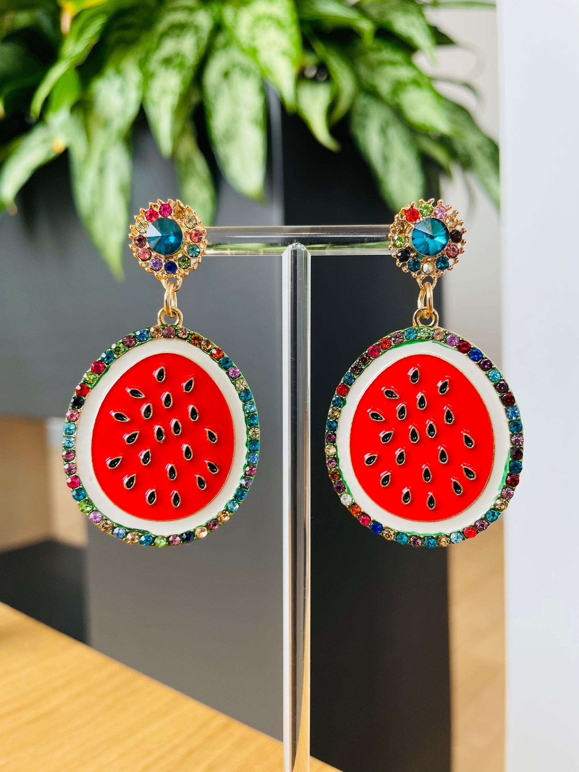 A pair of earrings designed to resemble watermelon slices, with a red center and green edges, adorned with small multicolored gemstones.